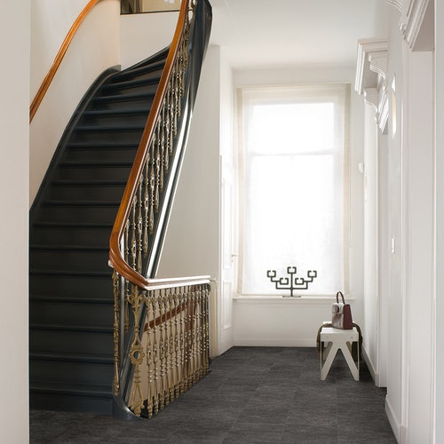 A hallway with a staircase and slate black laminate flooring.