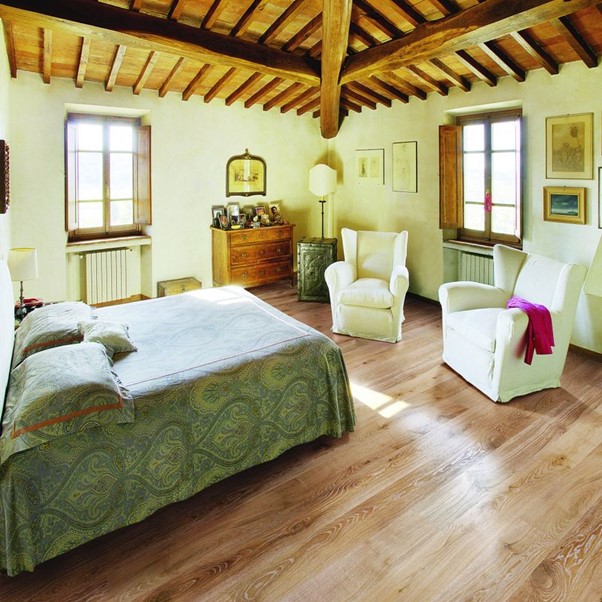 A bedroom with a bed, chairs and wooden flooring.