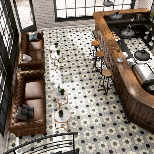 A room with two sofas, a bar with three bar stools and patterned tile flooring.