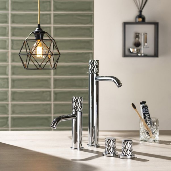 Two taps, a glass with a toothbrush and a geometric light feature with a tiled wall in the background.