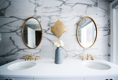 White ceramic sink with a marble tiled wall and two oval mirrors.