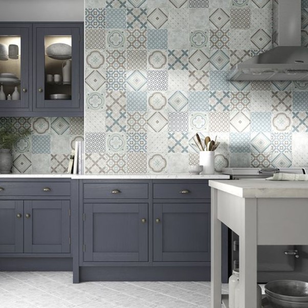 A kitchen with a white island, grey cabinets and patterned tile walls.