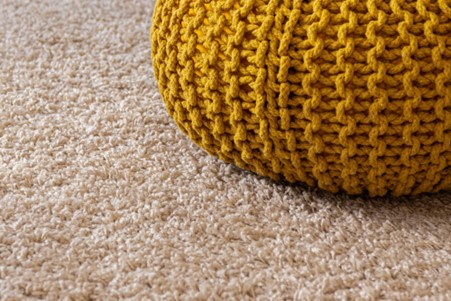 Yellow knitted footrest on fluffy carpet.