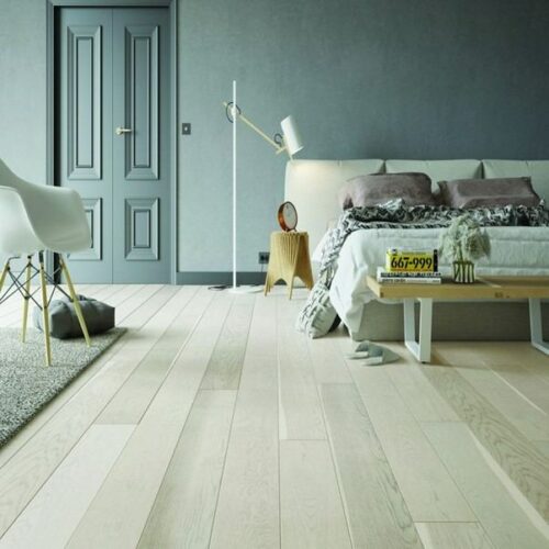 A bedroom with a bed, table and vertical, white wood effect flooring.