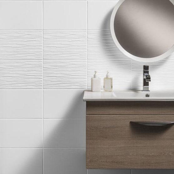 A wooden bathroom cabinet and basin with a round mirror and matt white wall tiles