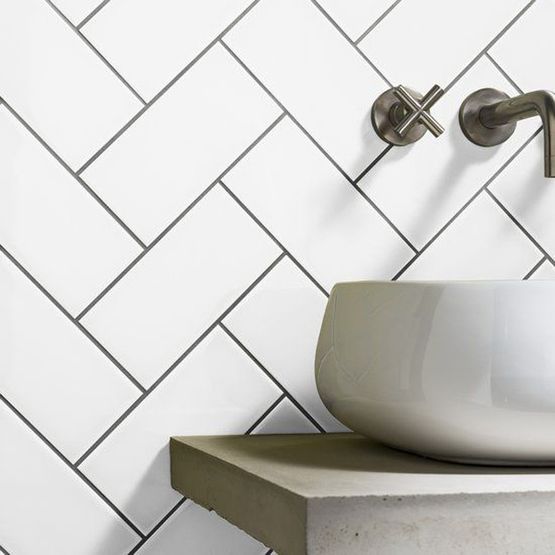 A bathroom sink with white rectangular tiles laid in a herringbone pattern