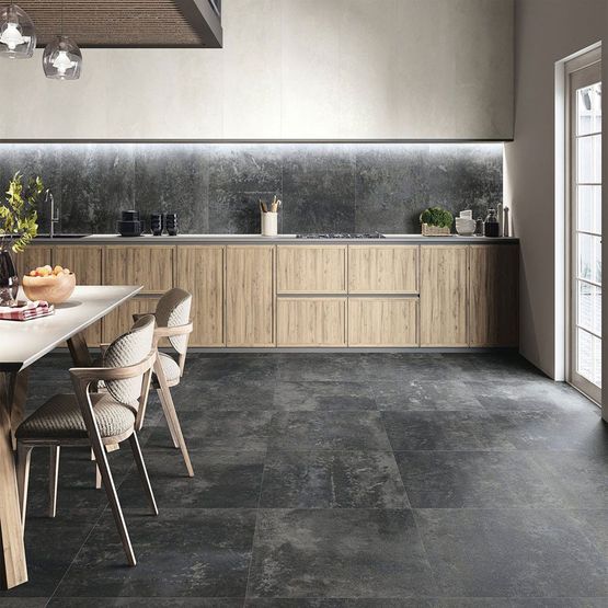A kitchen with dark grey stone effect porcelain tiles and light wooden cabinets