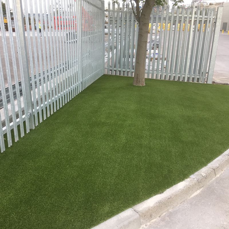 A tree next to a fence on a triangular artificial grass lawn. 