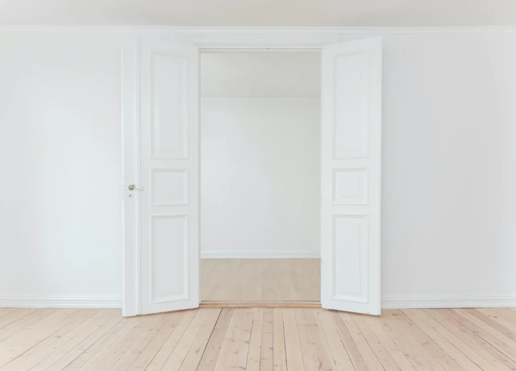 Laminate flooring with a transition bar between two white doors. 