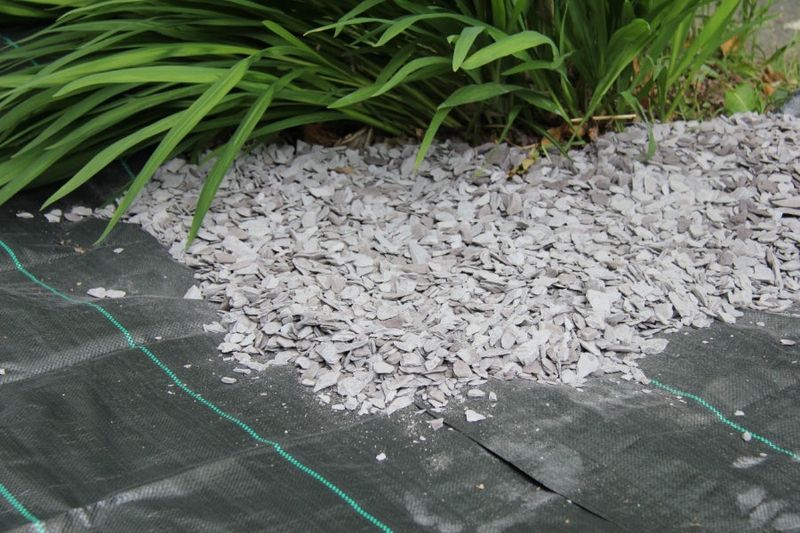 A pile of gravel on a fabric membrane next to a green plant. 