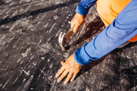 A person using a hammer on a wood subfloor board.