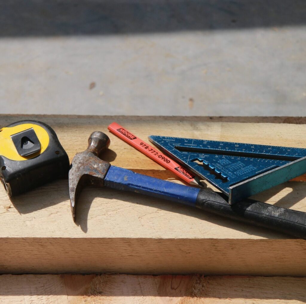 A hammer, tape measure pencil and right angle tool.