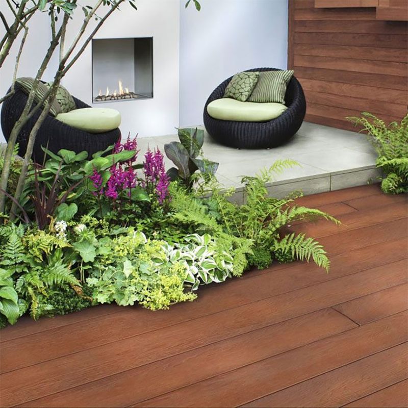 A patio with plants, chairs, decking and a fireplace.