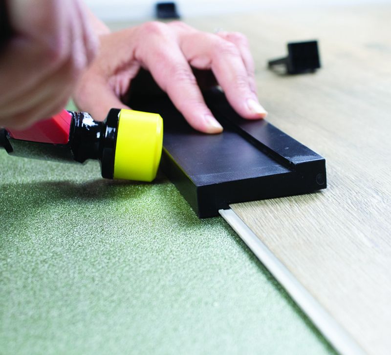 A person using a tapping block and hammer to install laminate flooring.