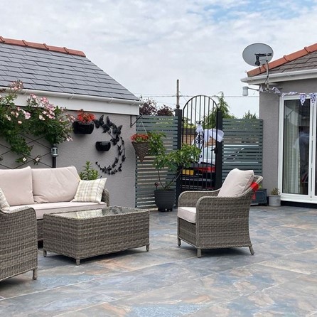 An outdoor space with grey rattan seating and slate effect floor tiles.