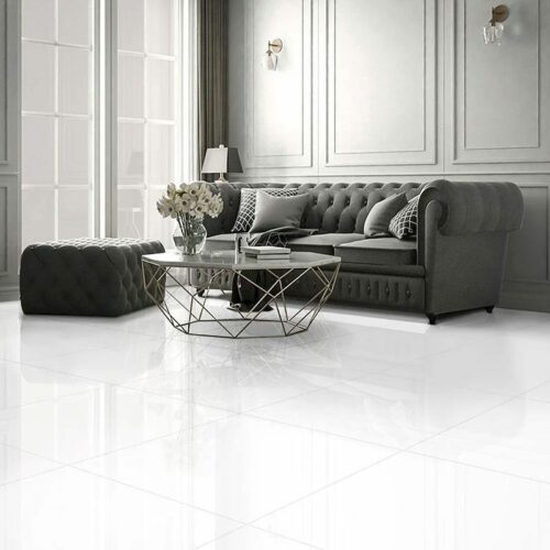 A living room with a sofa, coffee table and large white rectified tiles.