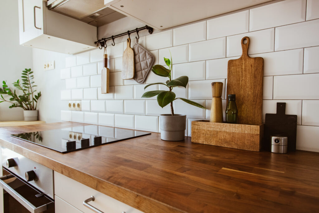 Kitchen brass utensils, chef accessories. Hanging kitchen with white metro tiles on the wall and splashback, and wood counter top. a green plant sits on top of it.
