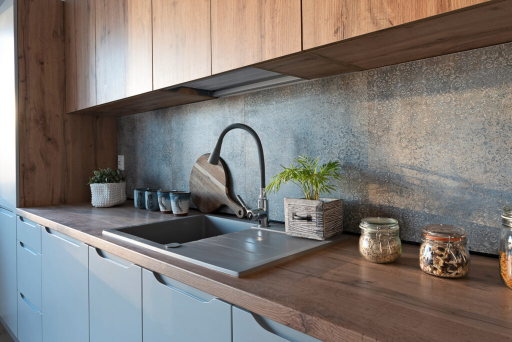 modern kitchen with natural wood cabinets and counter tops, with a dark baroque patterned splashback behind a matt grey sink